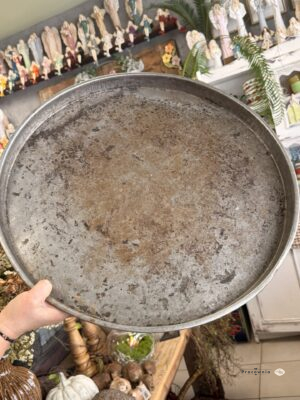 Vintage Taca - Okrągła taca dekoracyjna o średnicy 55 cm tworzy wspólną podstawę dla lampionów, wazonów i sezonowych ozdób. Metalowa powierzchnia w odcieniach szarości i brązu wyróżnia się przetarciami oraz efektem postarzenia, a niski rant otacza kompozycję. To propozycja do wnętrz rustykalnych, vintage i loftowych.