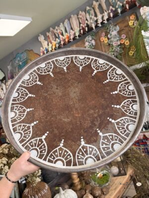 Vintage Taca XL- Taca dekoracyjna metalowa 55 cm brązowa z białym ornamentem. Okrągła taca dekoracyjna o średnicy 55 cm wyróżnia się brązową, postarzaną powierzchnią i białym ornamentem biegnącym wokół brzegu. Duży format oraz niski rant tworzą przestrzeń do wyeksponowania lampionu, wazonu i sezonowych dodatków. Pasuje do aranżacji boho, rustykalnych i vintage, w których liczą się ciepłe kolory oraz wyraziste wzory.